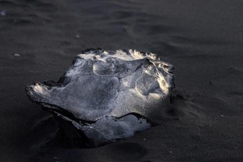 Gletschereis teilweise bedeckt mit schwarzem Sand