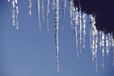 Eiszapfen am Dach vor blauem Himmel