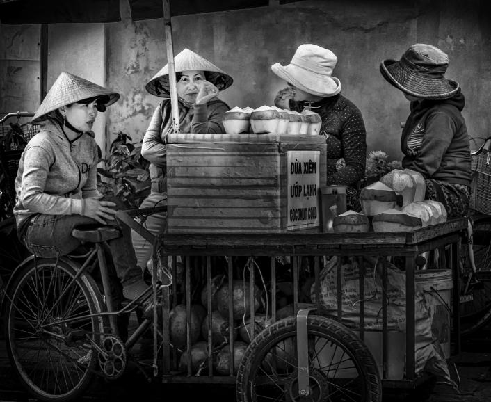 IDEE: Die Kokosnuss-Verkäuferinnen in Hôi An in Vietnam. Die vier Frauen unterhalten sich während ihrer Mittagspause miteinander und bilden mit
Wagen, Früchten und ihren Hüten eine Einheit. GESTALTUNG: Sehr gefallen die Wiederholungen der...