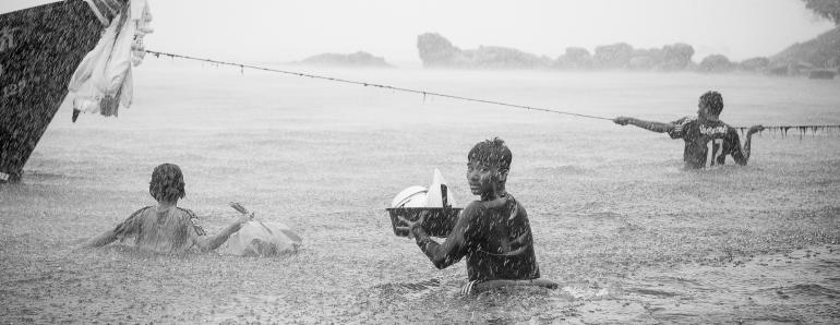 IDEE: Während eines Unwetters in Thailand bringen sich die Fischer auf ihren Booten ins Trockene – und müssen zunächst mit ihren
Habseligkeiten durch das Wasser waten. GESTALTUNG: Der Anschnitt deutet die Situation an – mehr muss man von Landschaft und
Boot nicht sehen. Toll der perfekte abgelichtete Regen und natürlich der Blick zurück. TECHNIK: Der bereits durchnässte Fotograf wagte sich aus seiner kümmerlichen Deckung und folgte den Fischern, um das einzige Foto – natürlich freihand – zu machen.