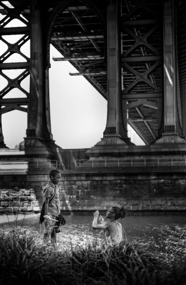 IDEE: Die monumentalen Pfeiler der Manhattan-Bridge bilden einen Widerspruch zu der leicht wirkenden Picknick-Szene unten.
GESTALTUNG: Die Schärfe liegt exakt auf den beiden diskutierenden Personen. Sehr gut gefällt das schräg einfallende Licht, das Mutter
und Sohn vom Hintergrund löst. TECHNIK: Zufallsfund auf der Brooklyn-Seite. Der Fotograf schlenderte durch den Park unter der Brücke. Spontan und freihand. 