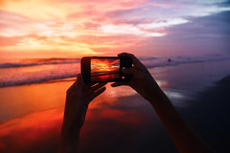 Mädchen nimmt ein Sonnenuntergangsfoto mit dem Handy auf.