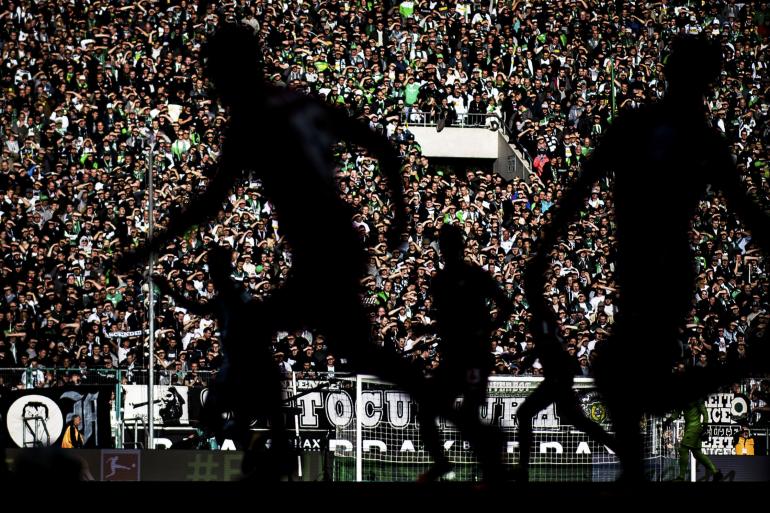 Spieler von Borussia Mönchengladbach und Bayer 04 Leverkusen zeichnen sich vor der von der Sonne angestrahlten Tribüne als Silhouetten ab. Schattenspiel | Nikon D5 | 105mm | 1/8000 s | f/1,4 | ISO 50 | 21.10.2017