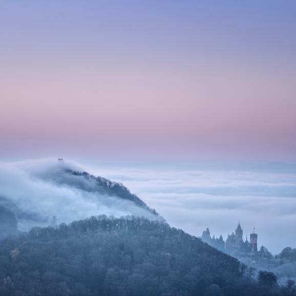 Der Blick vom Petersberg auf den Drachenfels und die Drachenburg im Siebengebirge: Diese Aufnahme entstand kurz vor Sonnenaufgang am frühen Morgen. Die Landschaft wurde durch eine Inversionswetterlage, mit ihren typisch tiefliegenden Wolken, geheimnisvoll in Nebel gehüllt. Sony Alpha 7 M3 | FE 70–200mm F4 G OSS | 118mm | 1/10 s | f/13 | ISO 100