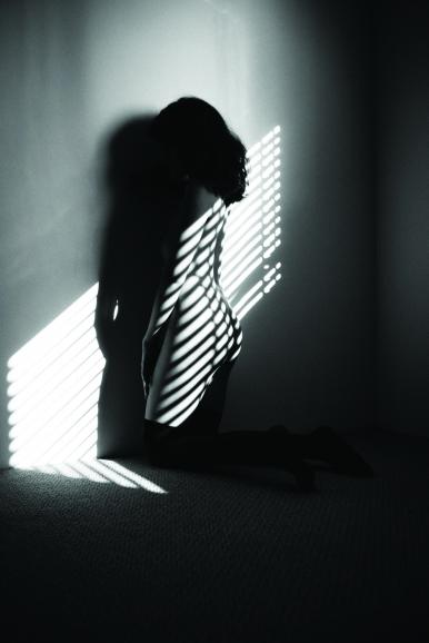 Durch die leicht geöffneten Jalousien fällt hartes Tageslicht ins Zimmer. Das Model wird direkt in den Lichtkegel positioniert, wodurch ein starker Kontrast aus Licht und Schatten entsteht.